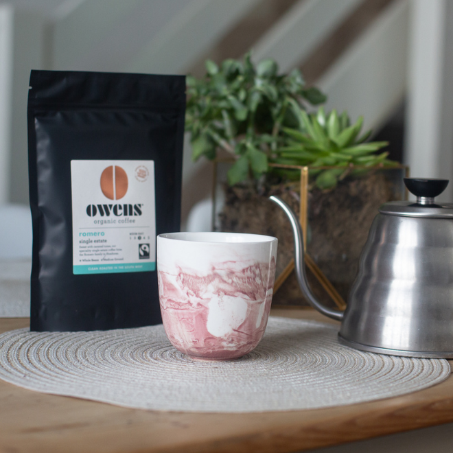 A bag of Romero coffee with a coffee cup and pouring kettle for filter